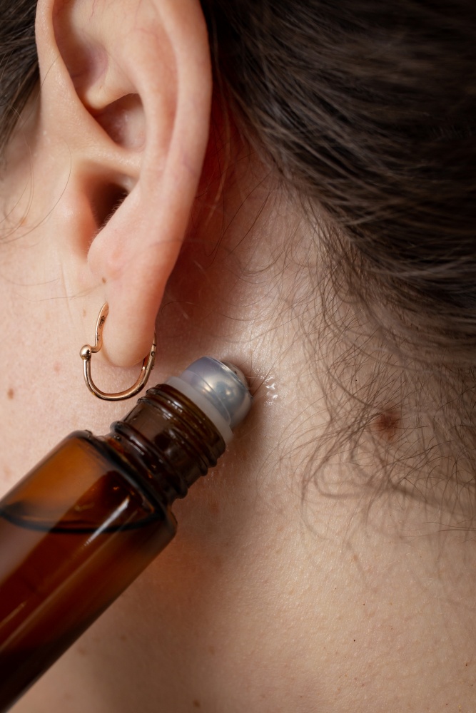 O femeie aplica in spatele urechii parfum sub forma roll-on
