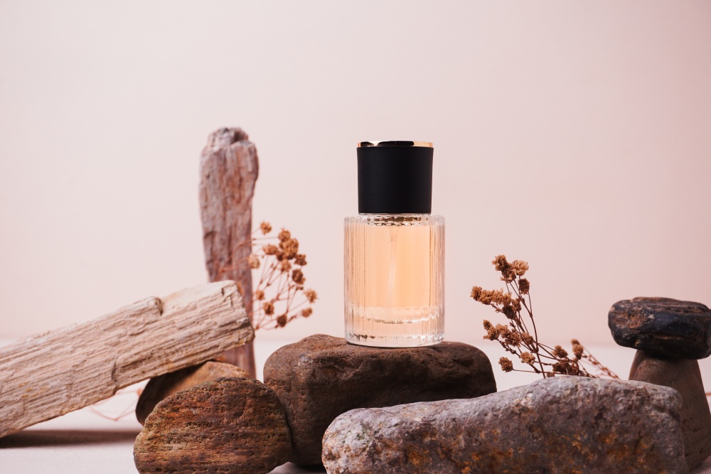 O sticla de parfum asezata intr-un decor natural cu lemn, piatra si flori, intr-un studio