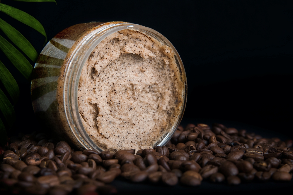 un borcanas de scurb asezat pe multe boabe de cafea si o panta verde in spate, fundal negru