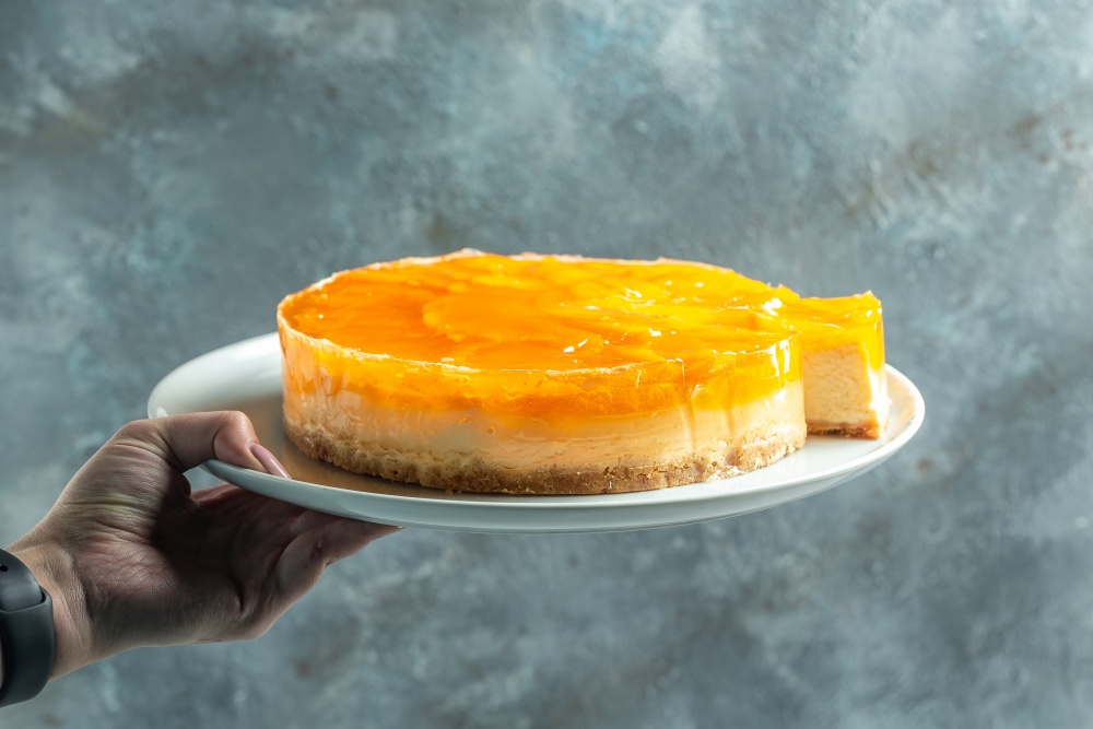 Mana unei persoane ce tine un platou cu cheesecake cu piersici