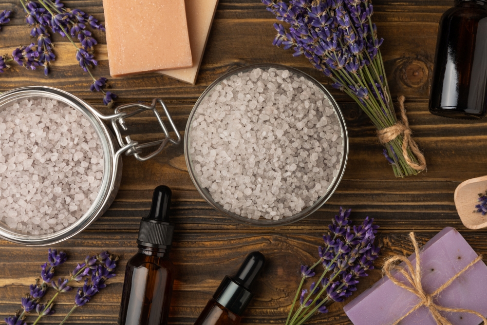 doua recipiente cu sare de mare, lavanda, uleiuri esentiale pe o masa de lemn maro