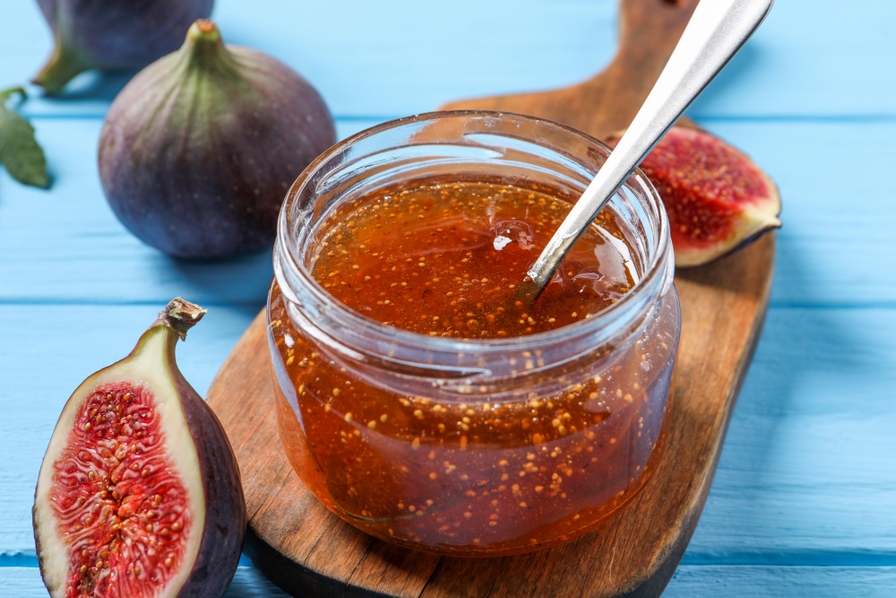 Un tocator de lemn pe care se afla un borcan cu dulceata de smochine si smochine proaspete