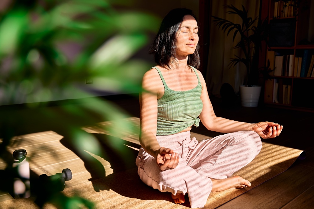 O femeie maditeaza si practica yoga intr-o camera luminoasa, lumina naturala si atmosfera relaxanta.