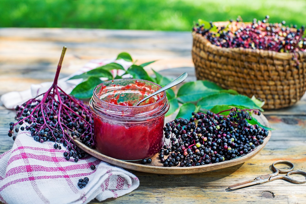Un borcan cu dulceata sau gem de fructe de soc alaturi de fructe coapte de soc si un servet de bucatarie