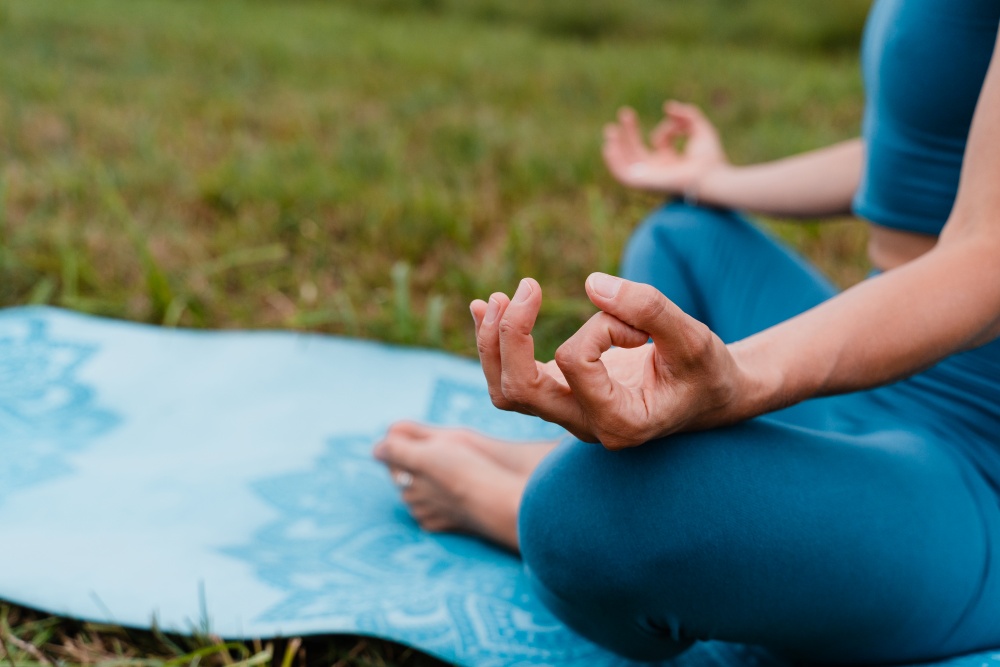 O persoana sta in pozitie de meditatie pe o saltea de yoga si practica Vayu Mudra