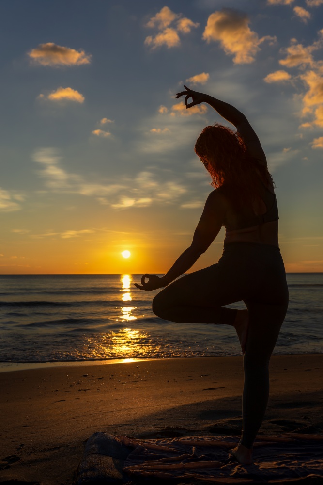 O femeie practicand yoga pe malul marii, la apus