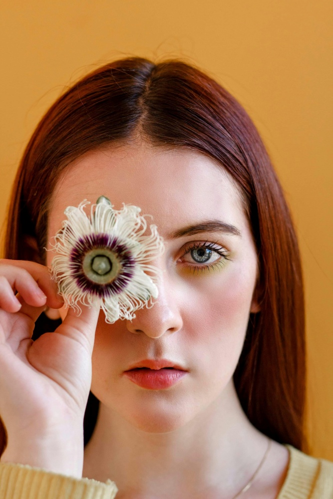 O femeie tina in dreptul ochiului o floare de passiflora