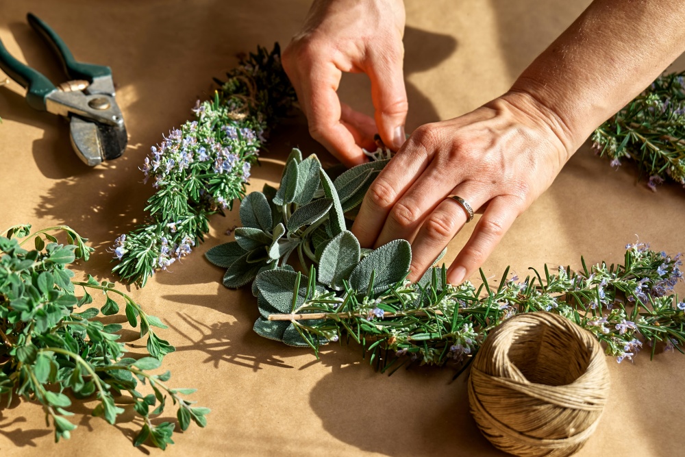 O femeie pregateste mai multe plante medicinale pentru uscare. Atmosfera luminoasa, mai multe plante medicinale se afla e o masa in bataia soarelui.