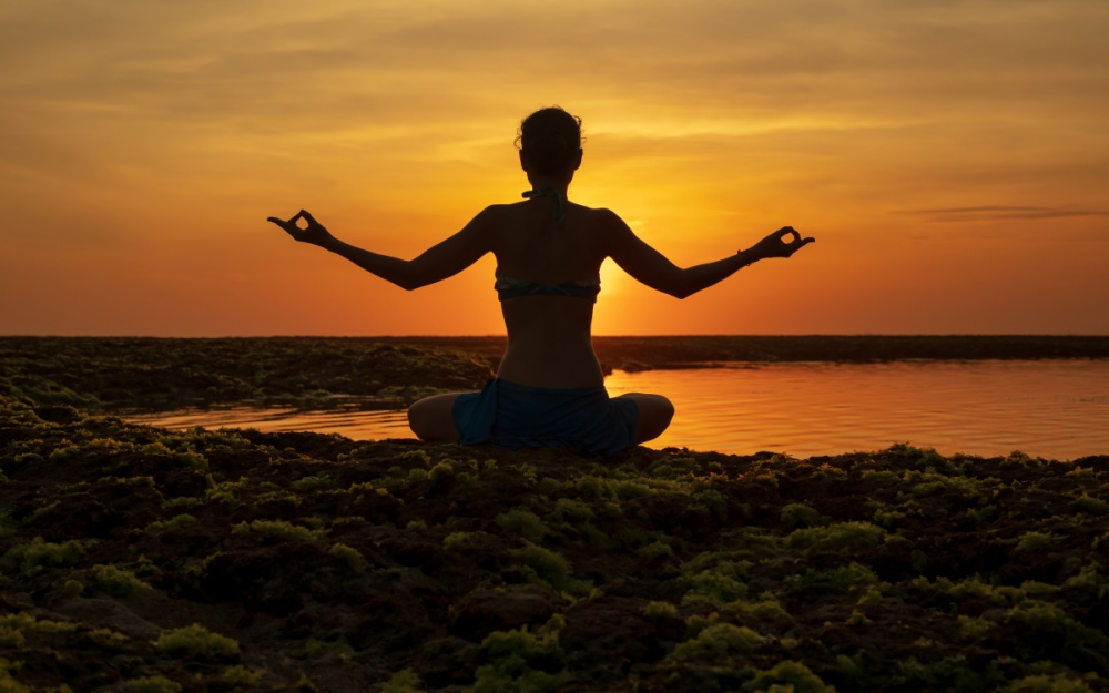 Silueta unei femei pe plaja, in pozitie de meditatie, practicand Gyan mantra
