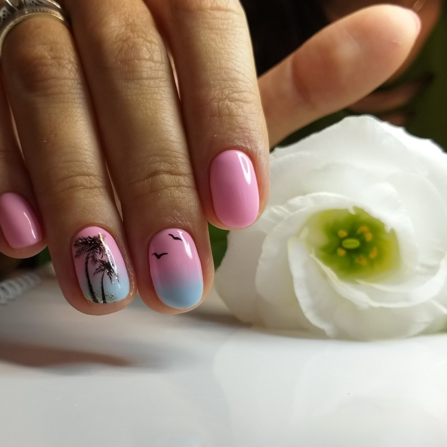 Manichiură gradient realizată cu ojă pastelată roz și bleu cu desen tropical imprimat 