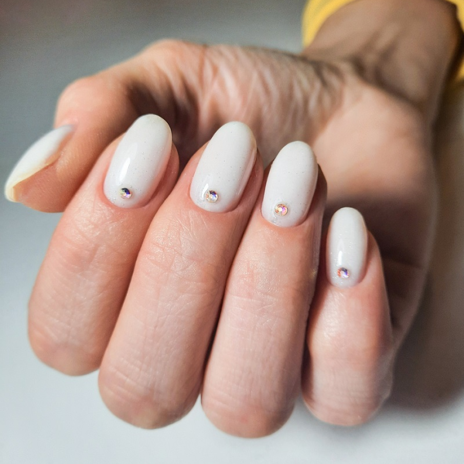 Manichiură albă cu ștrasuri aplicate la baza unghiei 