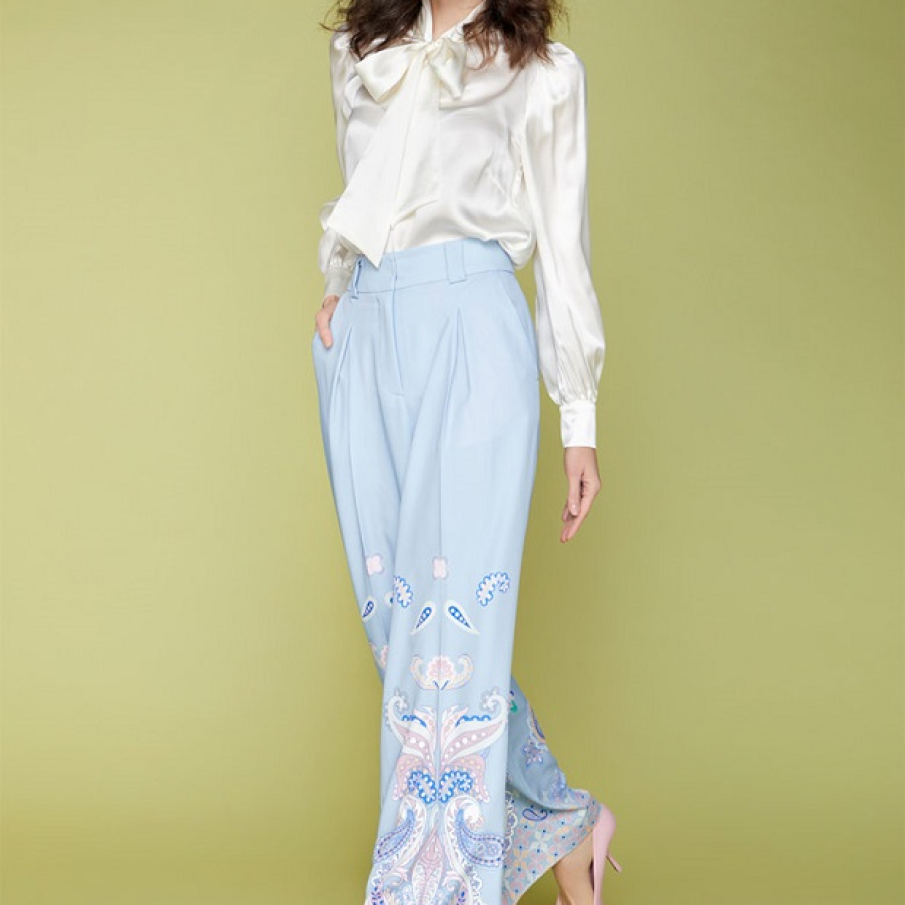 Pantaloni ampli în nuanță de albastru pastel, cu imprimeu etnic pe jumătatea lungimii lor, confecționați din satin, un material subțire. 