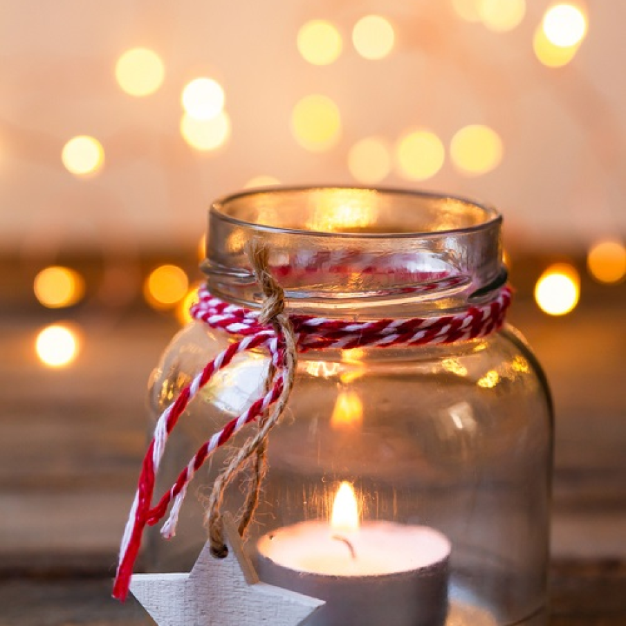 Decorațiune luminoasă homemade cu lumânare plasată într-un borcan decorat cu panglică roșu cu alb și sfoară, la capătul căreia este atârnat o steluță