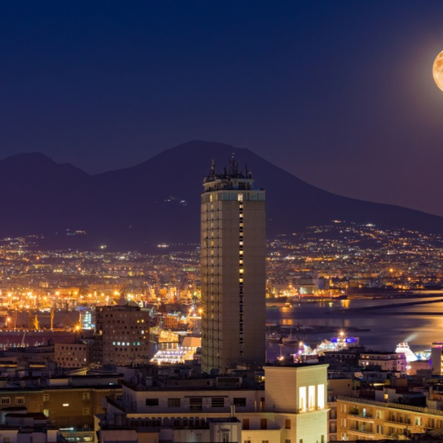 Luna plina se reflecta duios in apele calme ale marii.  Imaginea surprinde luna plina deasupra muntelui Vezuviu si a orasului Napoli (Italia)