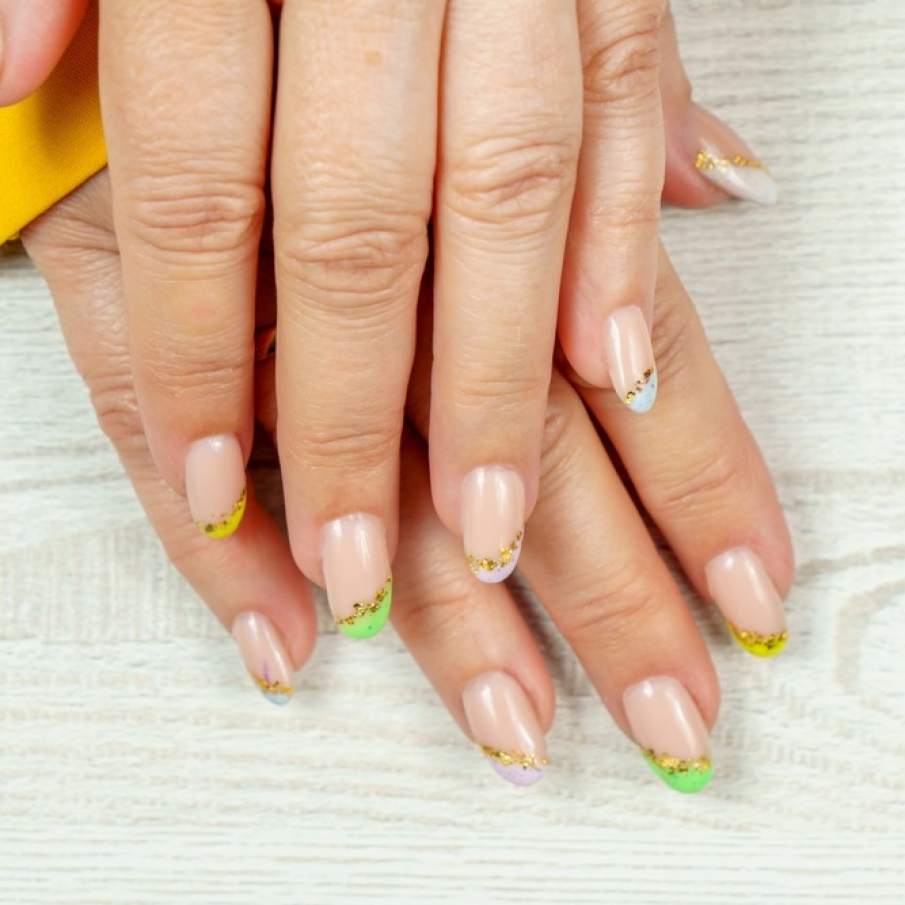 Manichiură franțuzească multicoloră, cu galben predominant, și delimitări gingașe și speciale realizate cu ajutorul glitterului auriu aplicat