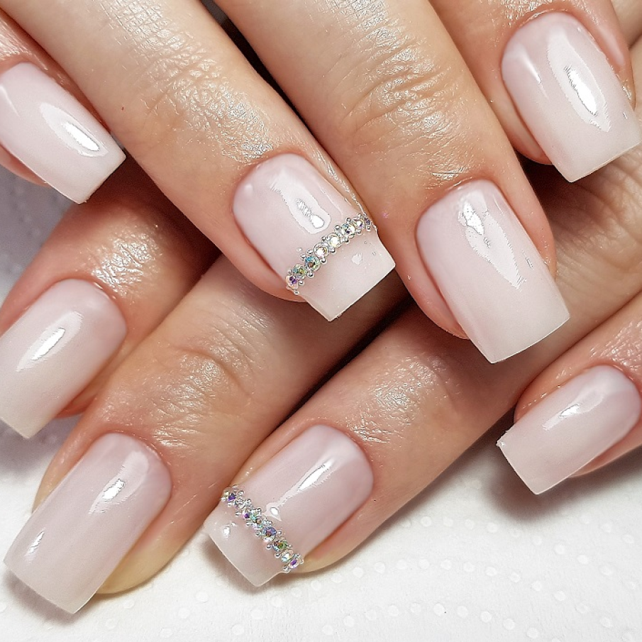 Model de unghii în nuanță de alb lăptos decorat cu ștrasuri transparente și multicolore 