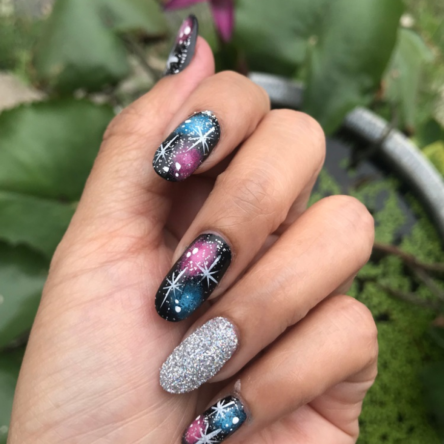 Manichiură picturală tip galaxie, cu accente de strălucire și stele pictate pe unghii