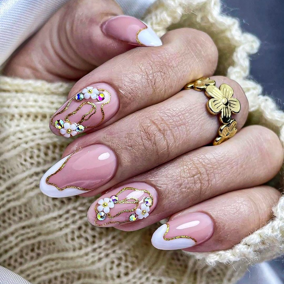 Manichiură nail art în stil franțuzesc, cu glitter și floricele aplicate alături de ștrasuri strălucitoare 