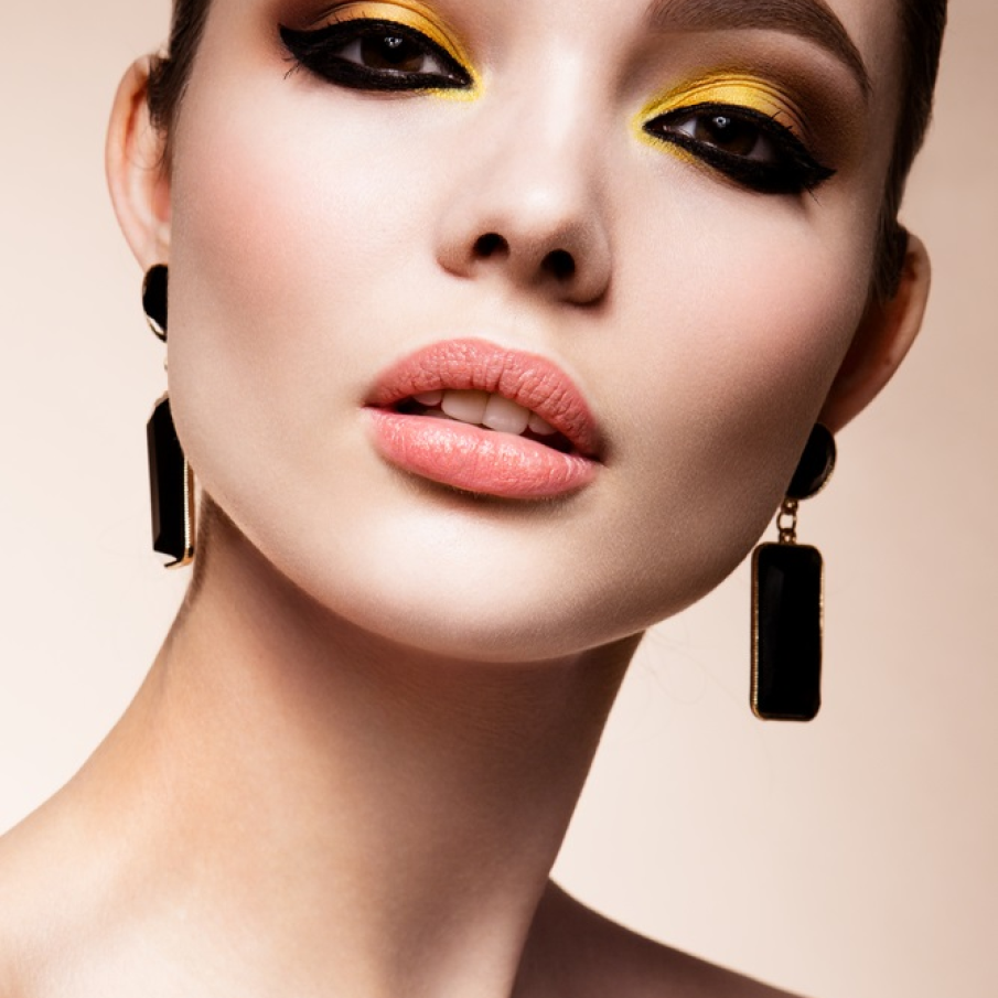 Machiaj sexy, stil cât-eye, cu dungi groase și bine pronunțate de tuș pentru a scoate în evidență ochii căprui. Negrul intens contrastează minunat cu galbenul solar al fardului de pleoape