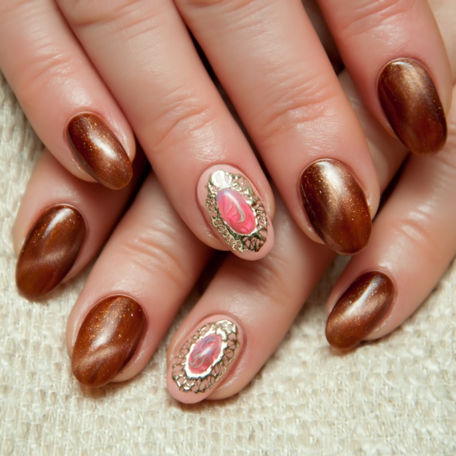 Manichiura Ochi de pisică în nuanțele ciocolatei cu lapte, cu un detaliu tip broșă pe unghia inelarului. 