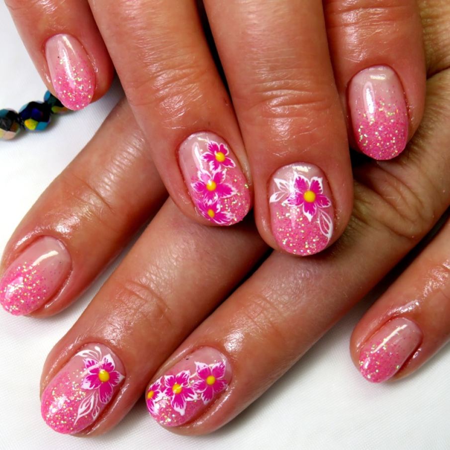 Manichiură cu gel cu glitter predominant roz, cu particule aurii și multicolore și flori stanțate 