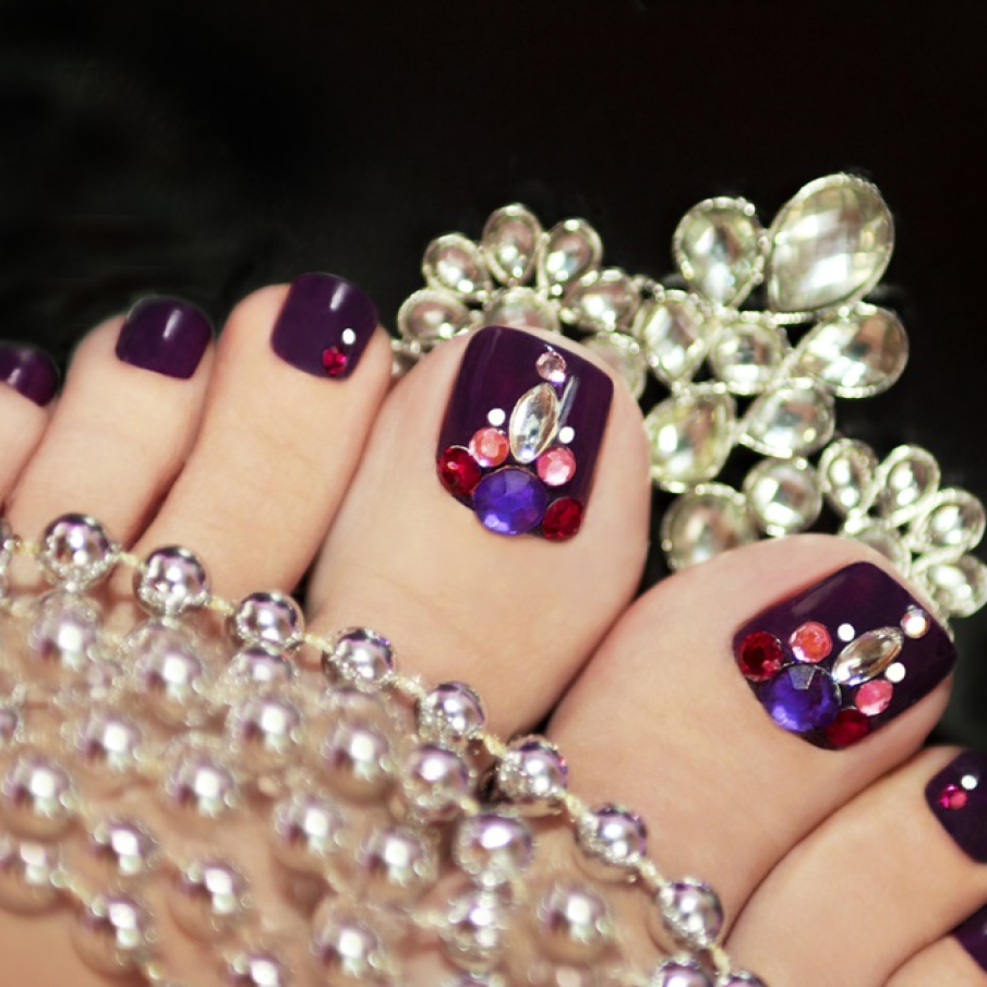 Pedichiură violet opulentă și exuberantă, elegantă, cu pietre și ștrasuri multicolore aplicate pe unghia mare și unghia alăturată