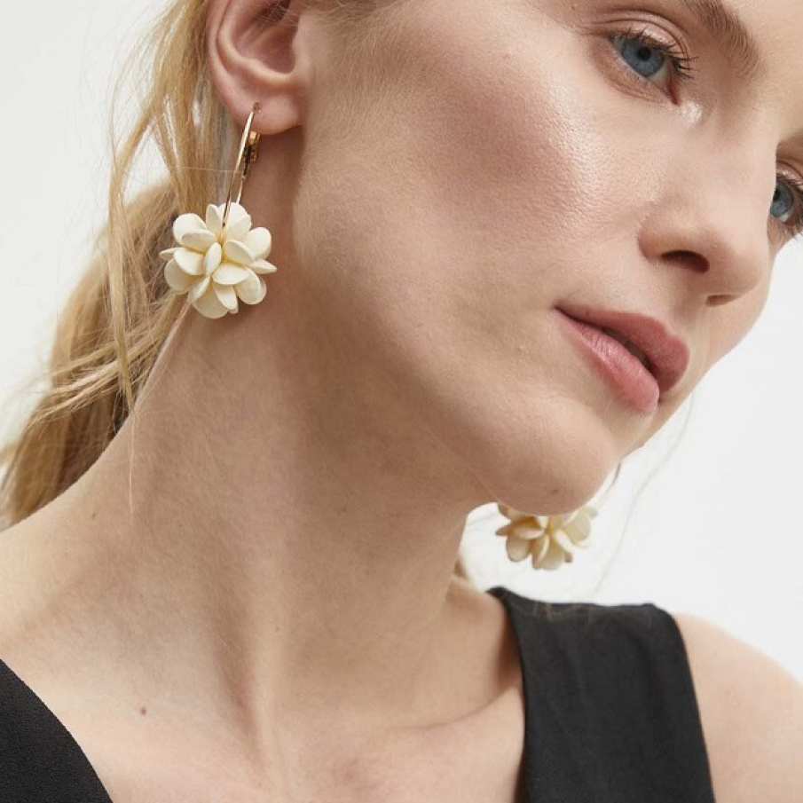 Cercei rotunzi în stil hoops, placați cu aur, din colecția Answear Lab, de care sunt suspendați flori albe 