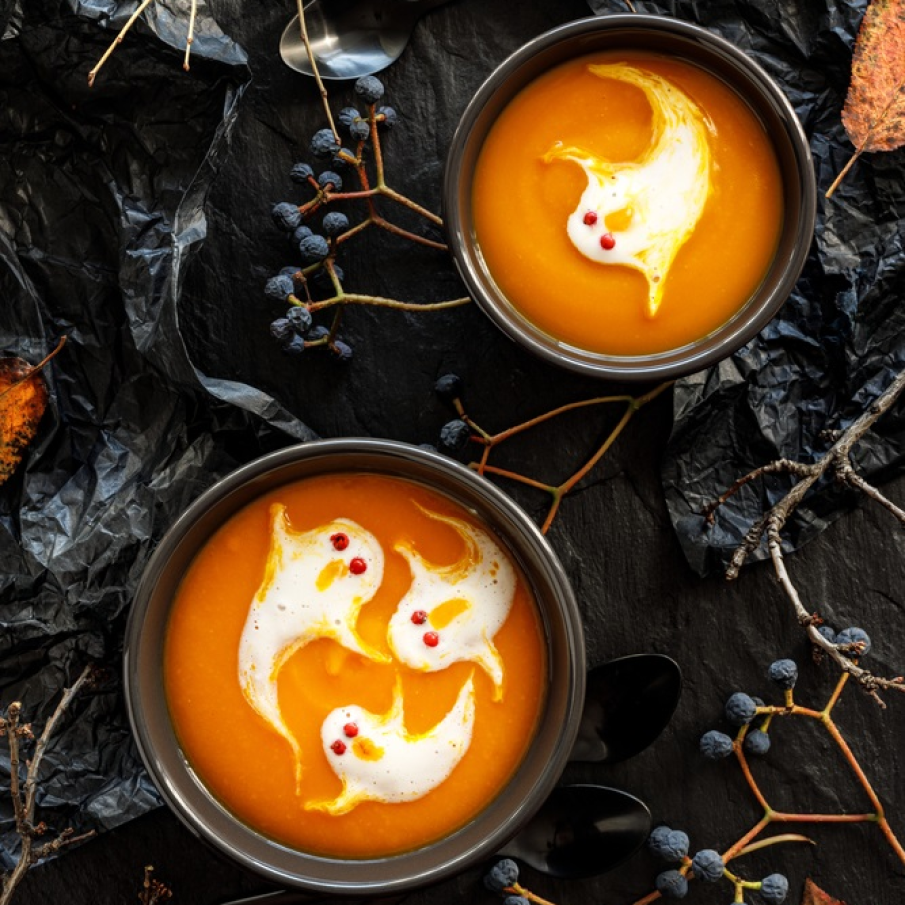 Supă de dovleac pentru Halloween decorată deasupra cu fantome realizate cu măiestrie din smântână 