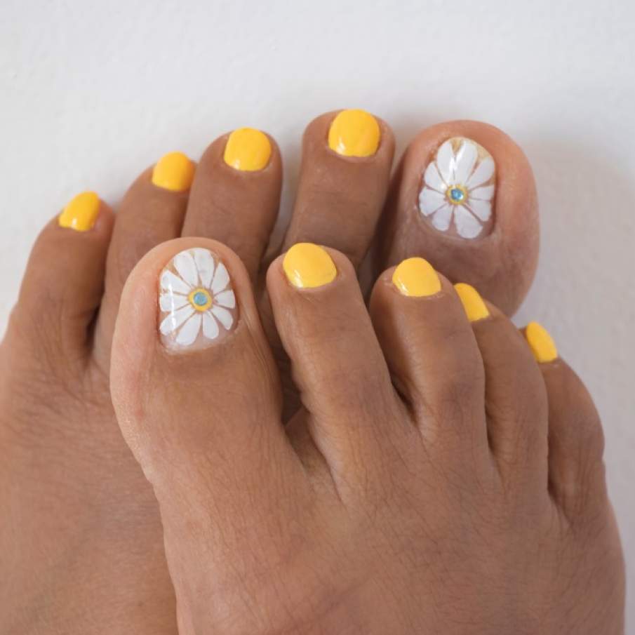 Pedichiură nail art în nuanță de galben solar, intens, cu o floare pictată pe unghia degetului mare 