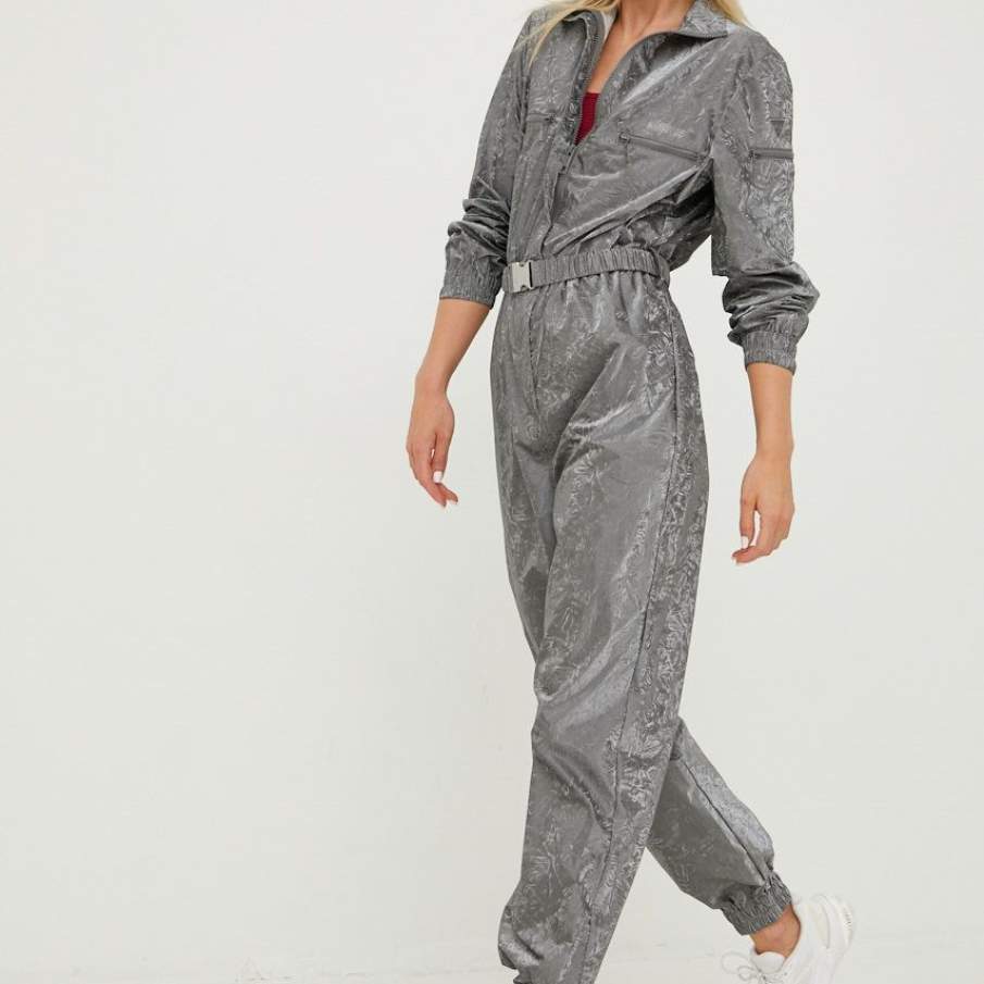 Salopetă sport casual în nuanță de gri, confecționată din textil. Dispune de bandă elastică în talie, iar piciorul pantalonului este finisat cu manșete