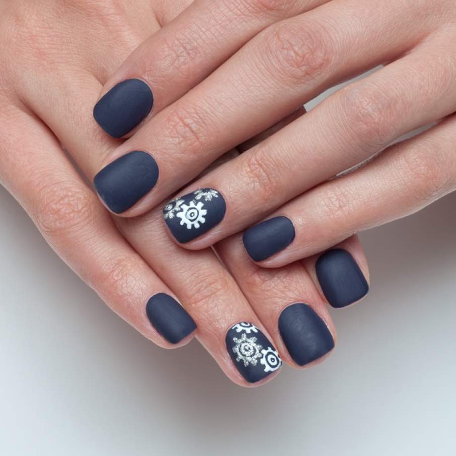 Manichiură în nuanță de albastru închis și rece, cu angrenaje albe pictate pe unghia arătătorului 