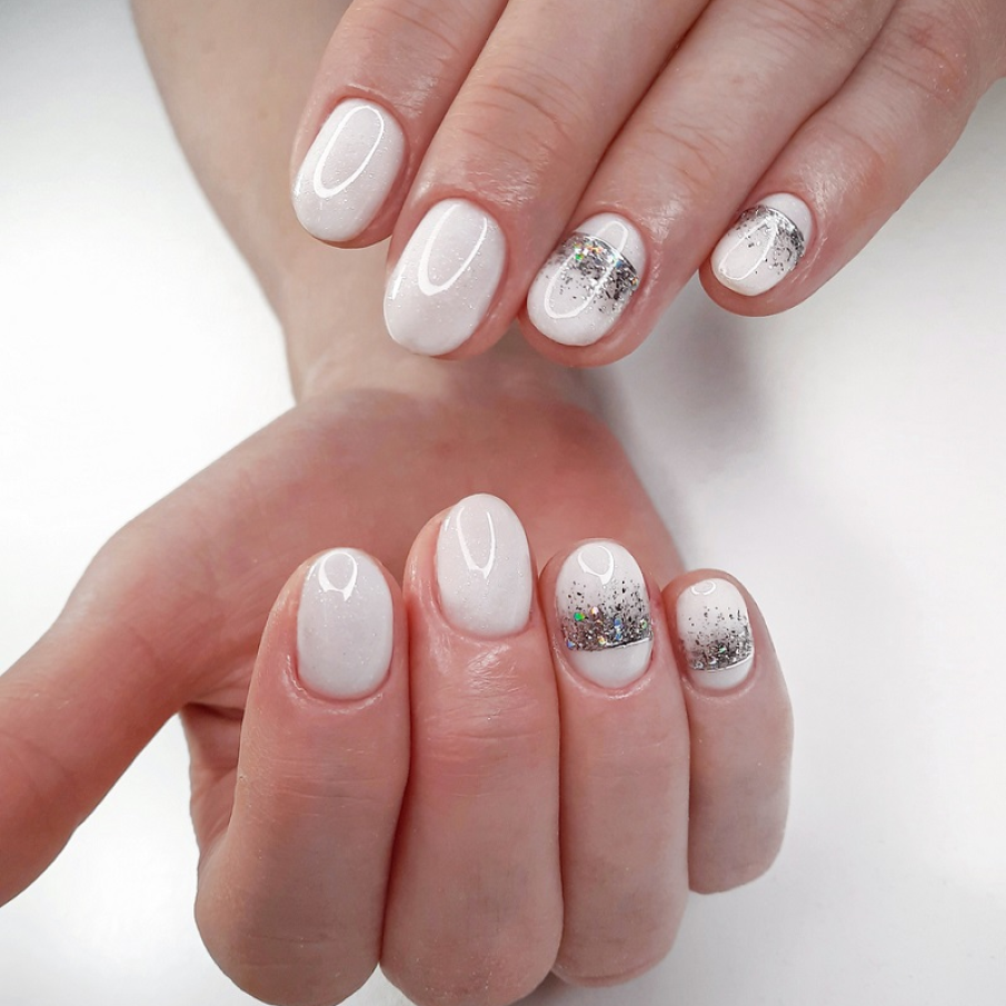 Manichiură albă strălucitoare cu detalii tip coroană, cu glitter argintiu strălucitor și particule multicolore pe unghiile a două degete