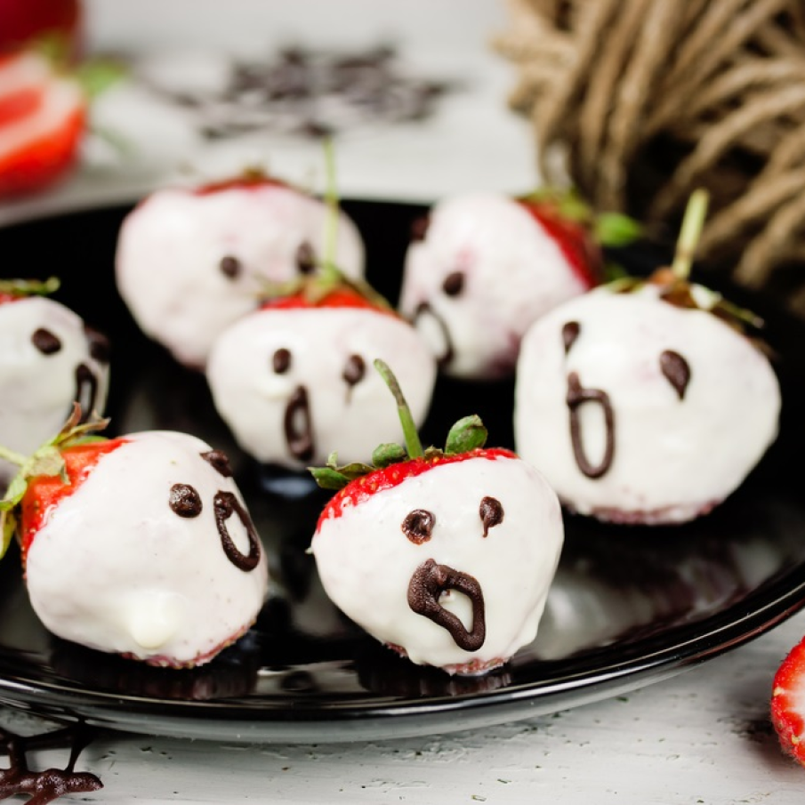 Căpșuni de Halloween trase prin ciocolată albă și decorate cu ochișori și gură pentru a reda înspăimântătoarele fantome