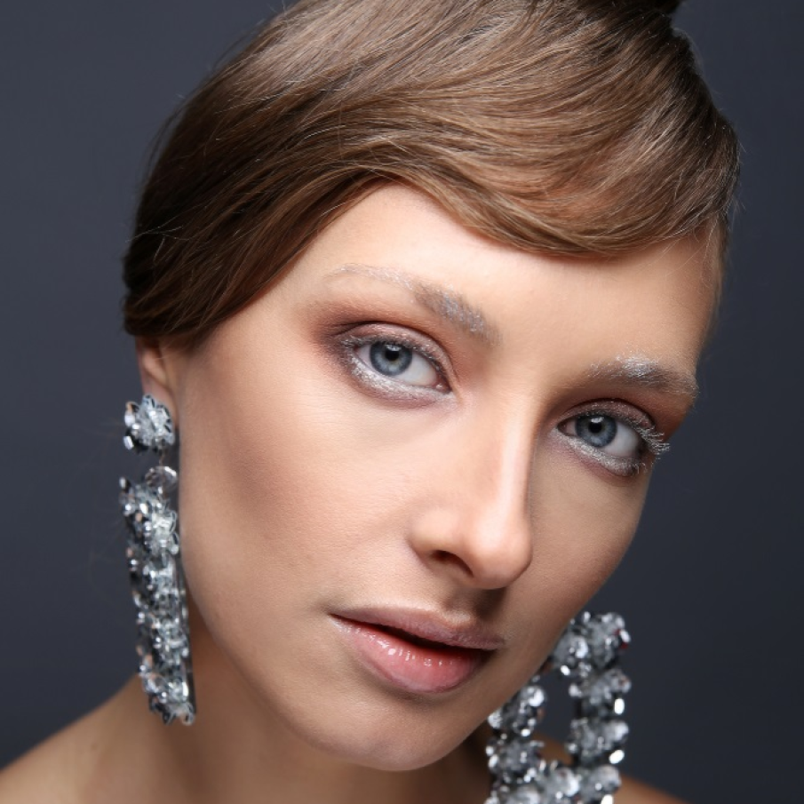 Machiaj festiv de iarnă pe bază de alb și glitter argintiu. Buzele sunt nude, iar accentul cade asupra tenului proaspăt, perfect 