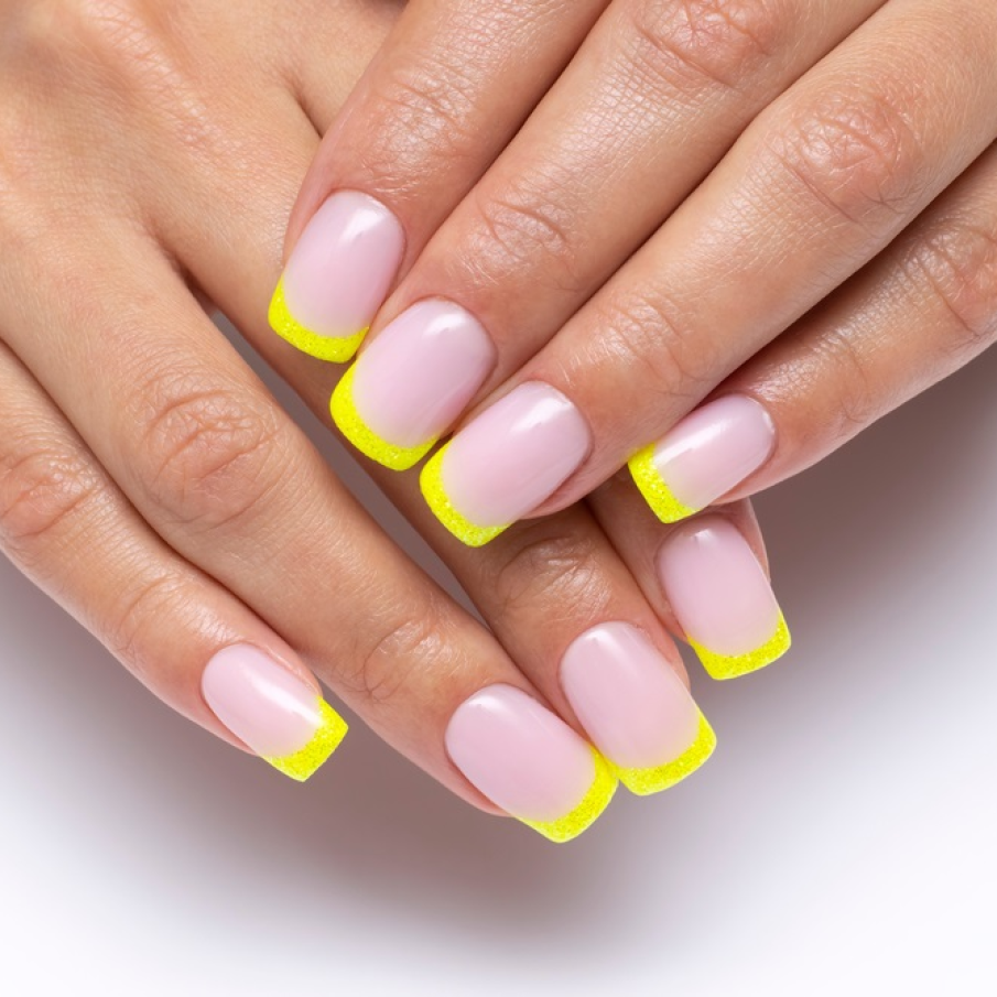 Manichiură franțuzească cu  unghiile de formă pătrată și vârfurile unghiilor pictate cu ojă galbenă cu glitter 