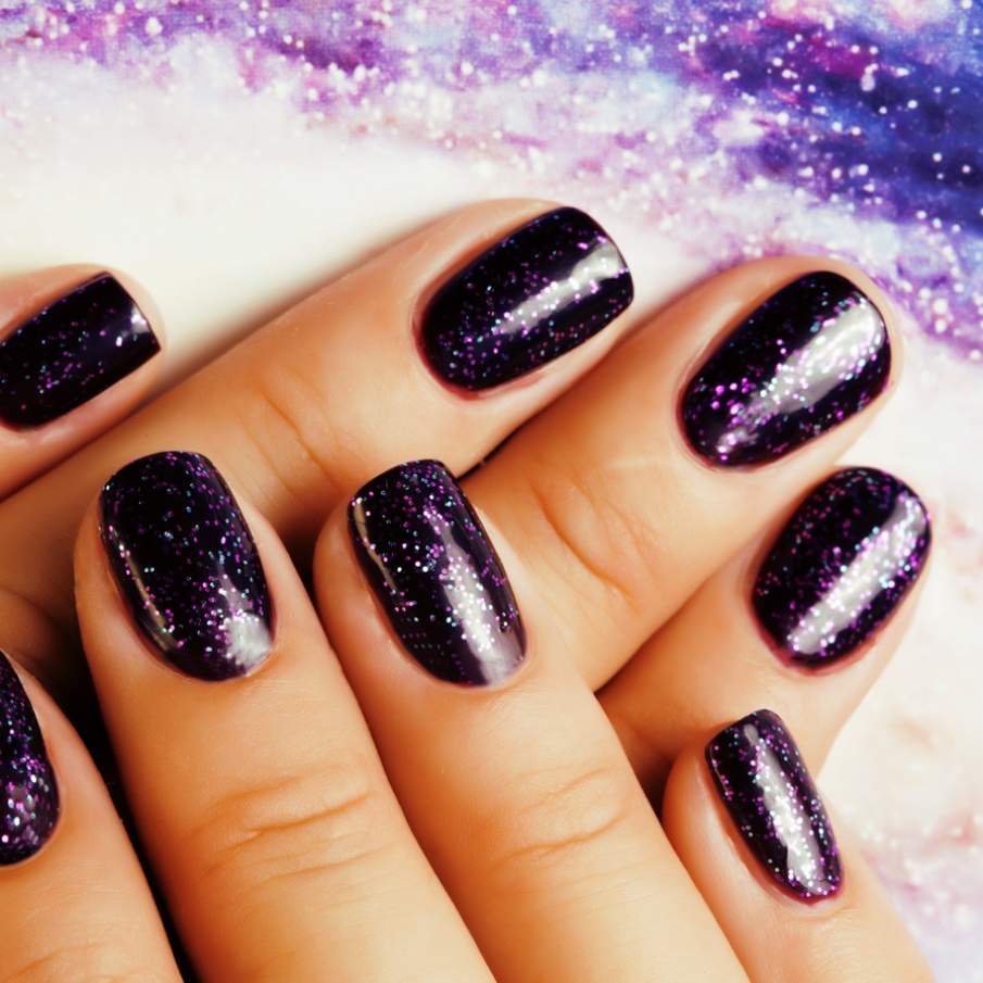 Manichiură dark space cu glitter violet, alb și bleu menit să recreeze efectul de spațiu incomensurabil 