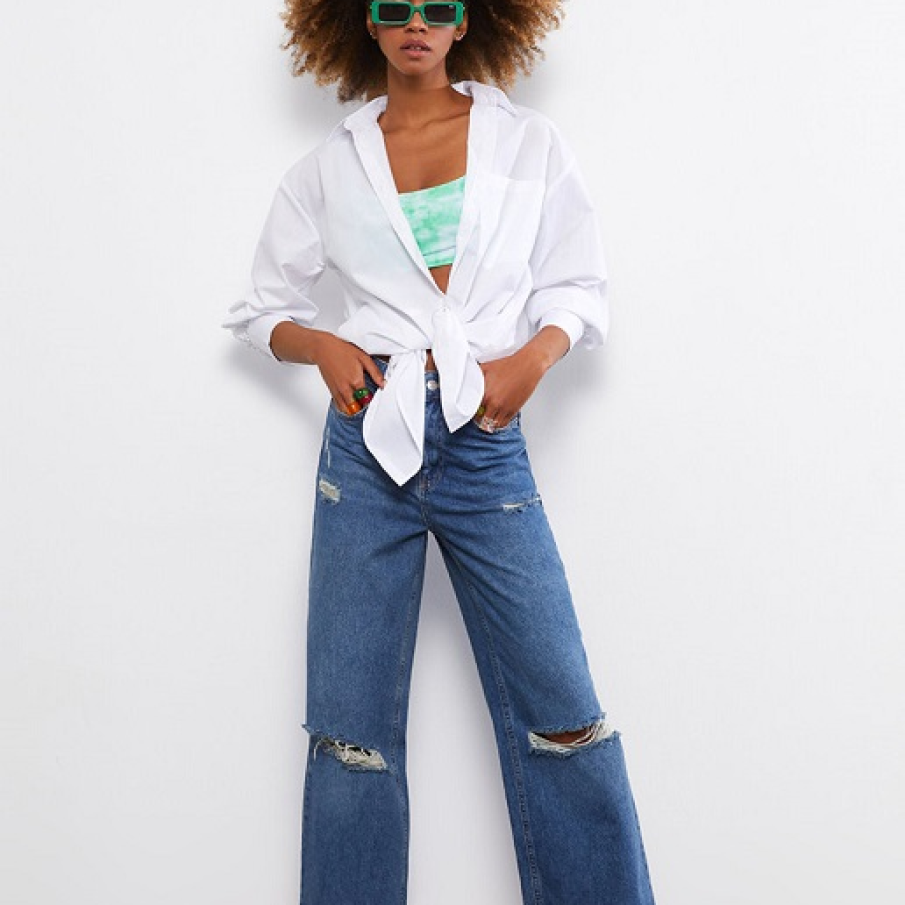 Blugi albastru închis cu talie înaltă, cu pantalon supradimensionat și detalii deteriorate pe alocuri. 