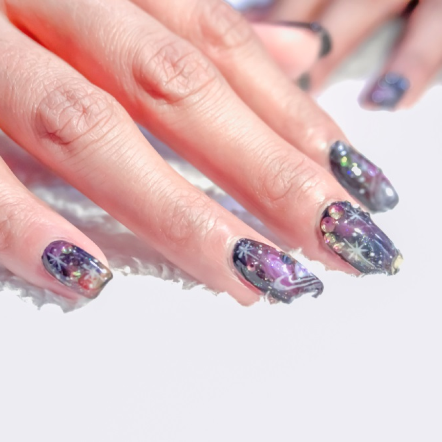 Manichiură galaxy decorată cu ștrasuri și glitter strălucitor 
