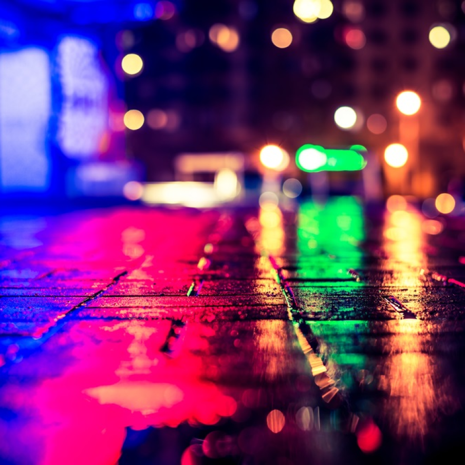Luminile multicolore ale unui club de noapte se reflecta in trotuarul ud