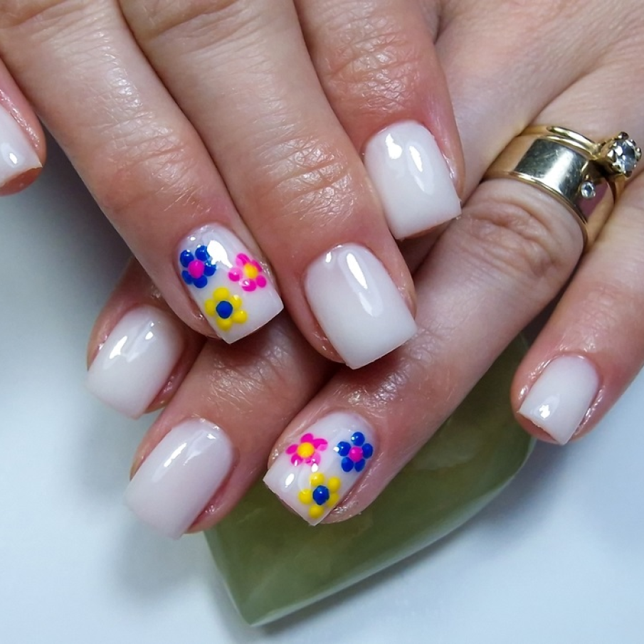 Manichiură alb lăptos strălucitor, cu o unghie pusă în evidență de flori multicolore pictate 