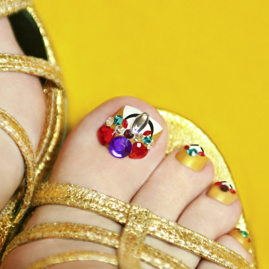 Pedichiură aurie, glamorous și sofisticată, cu cristale colorate aplicate, de diverse dimensiuni 